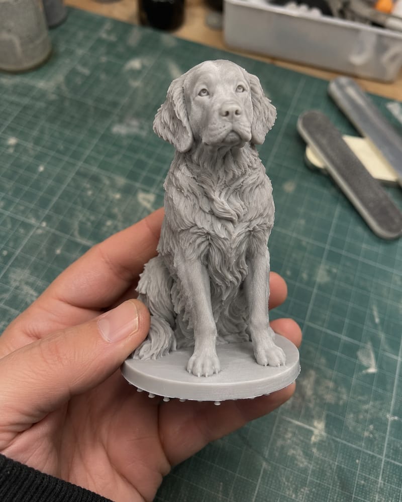 The unpainted grey resin print of the golden retriever held in a hand